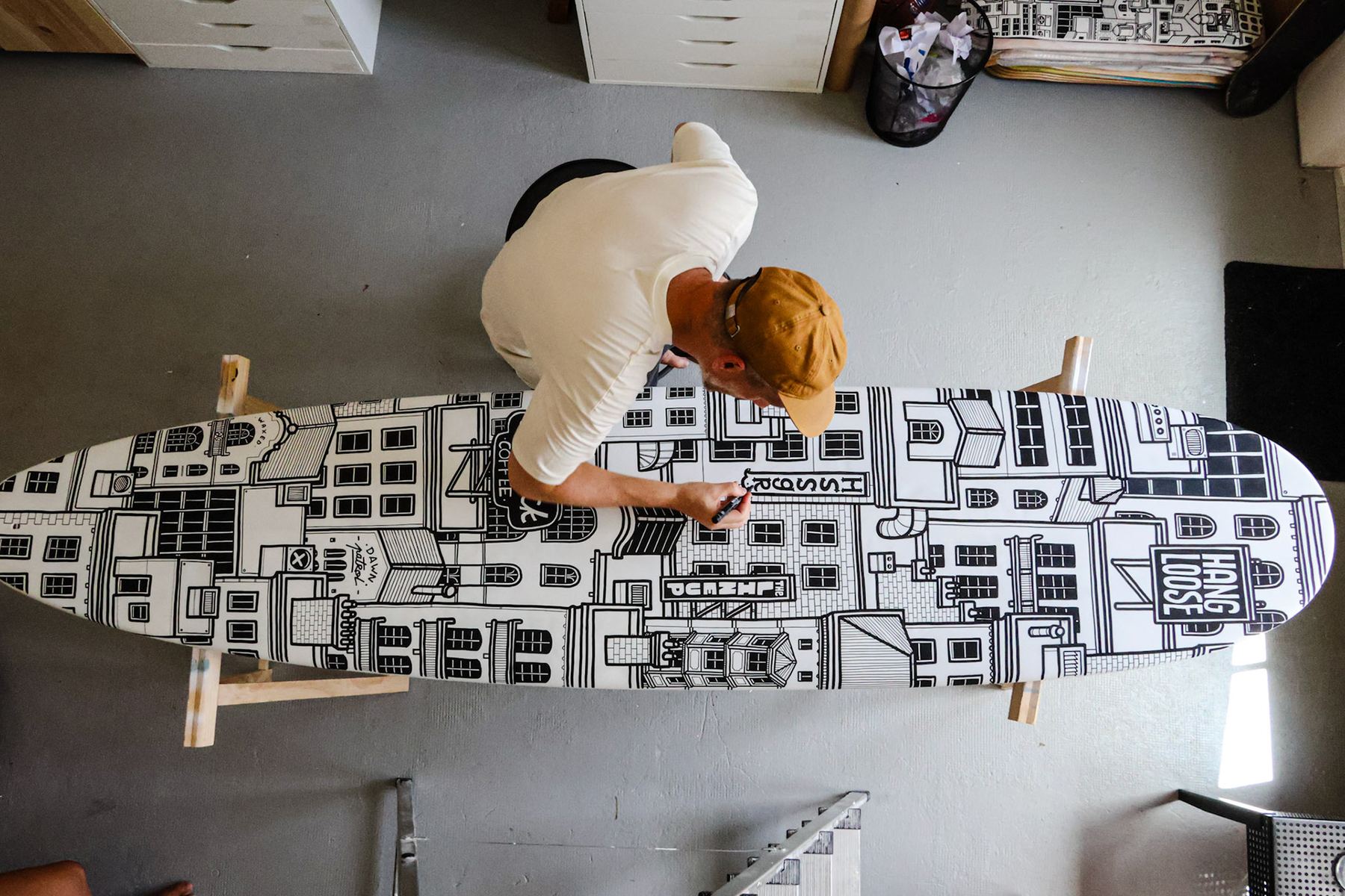 Vue plongeante sur l’illustrateur penché sur une planche de surf dessinée.
