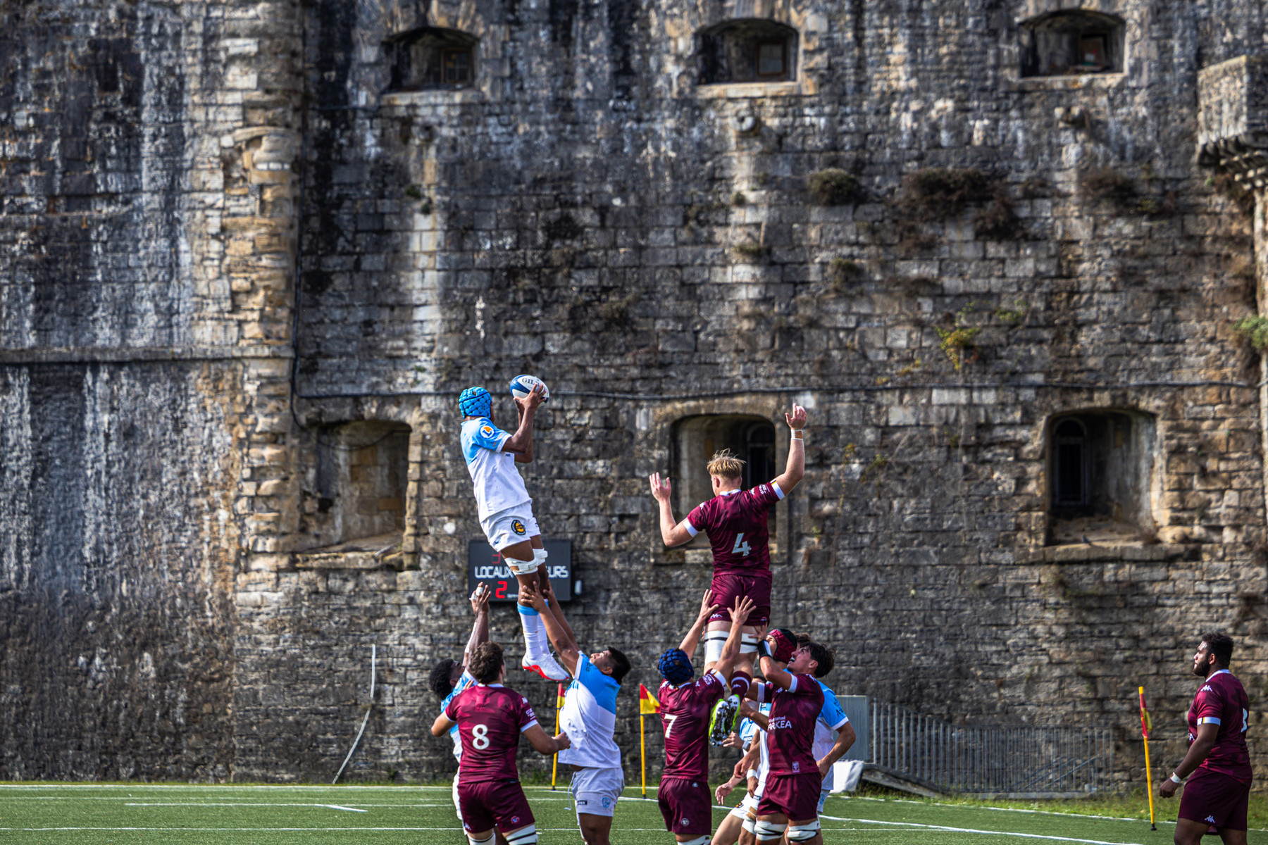Une touche disputée devant les remparts de pierre, joueurs bordelais en maillot bordeaux.